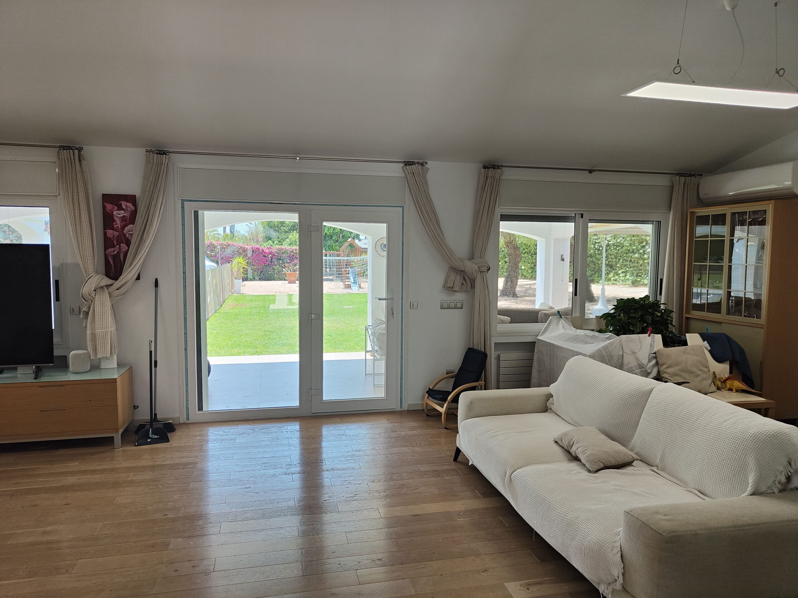 Salon con puerta balconera blanca y ventana que dan al jardin y a la piscina