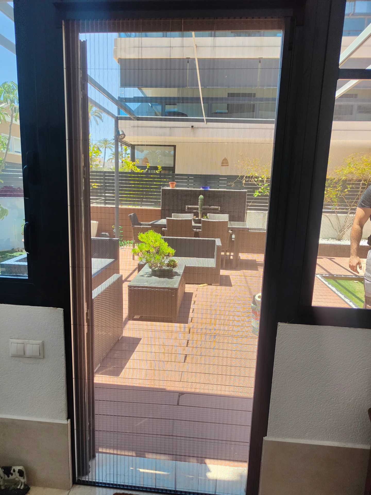 Salida a una terraza protegida con mosquitera plisada, vista desde el interior de la vivienda