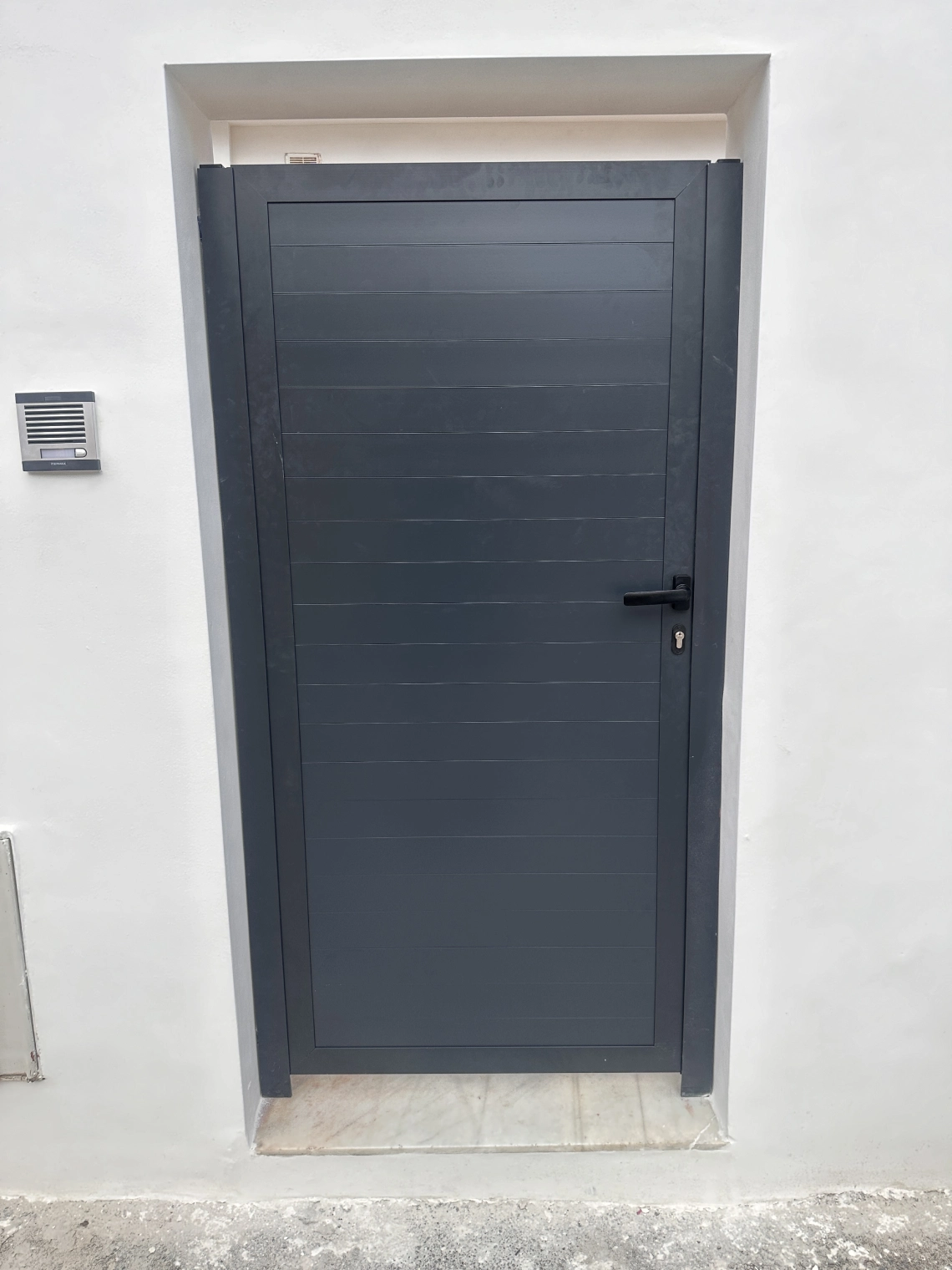 Puerta de aluminio lacado en gris antracita instalada en una fachada blanca