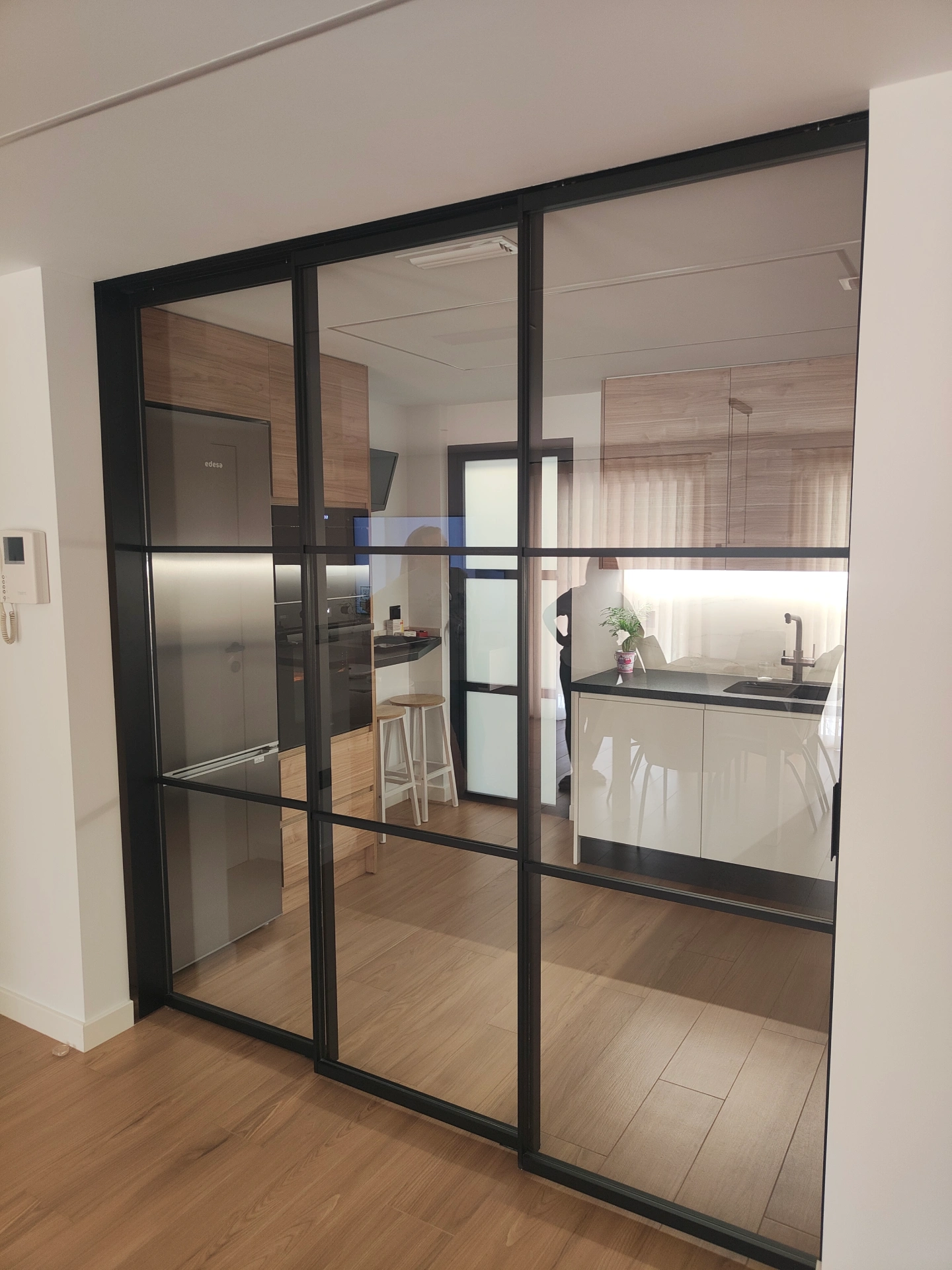 Separador de cristal con perfileria negra que divide la cocina del salon