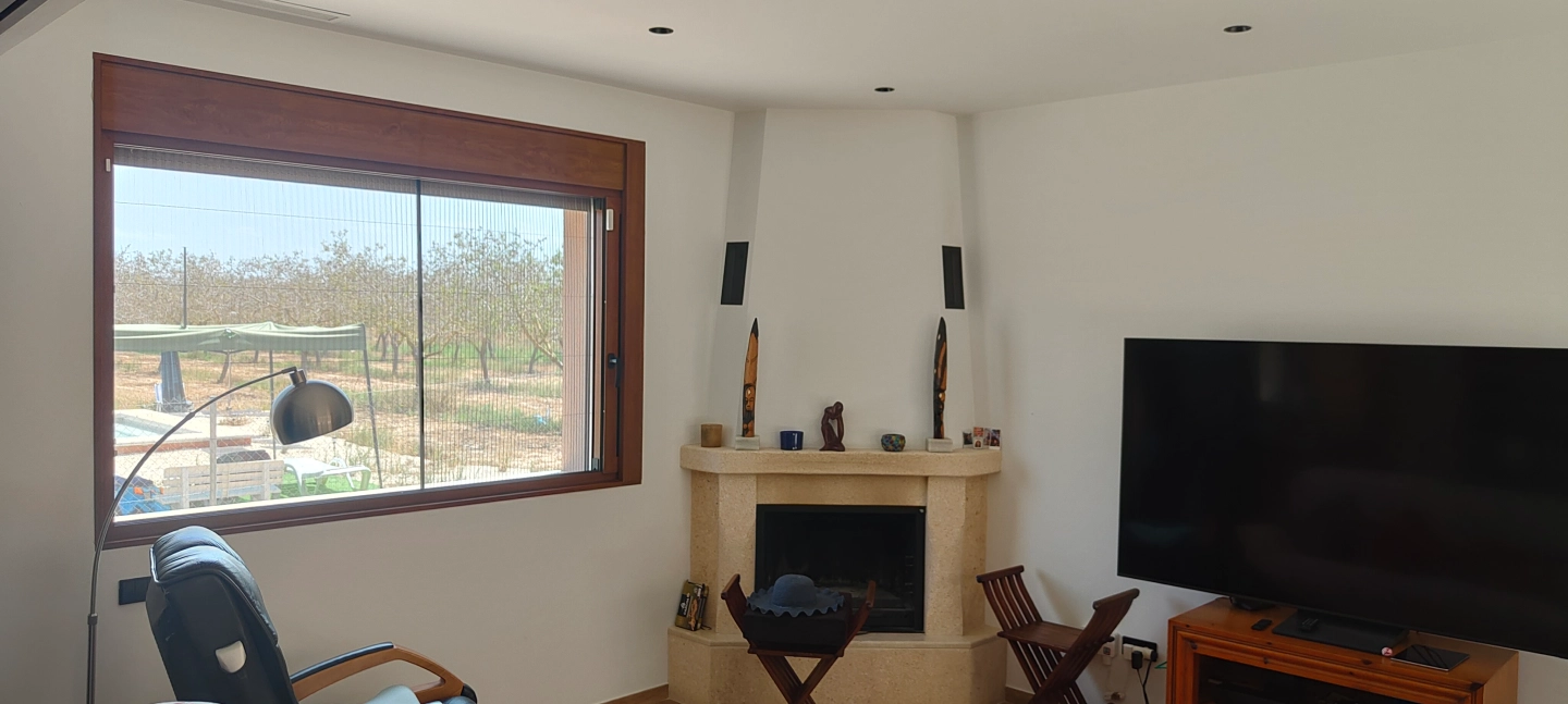 Salon con chimenea y ventana corredera de aluminio color madera con vistas al campo