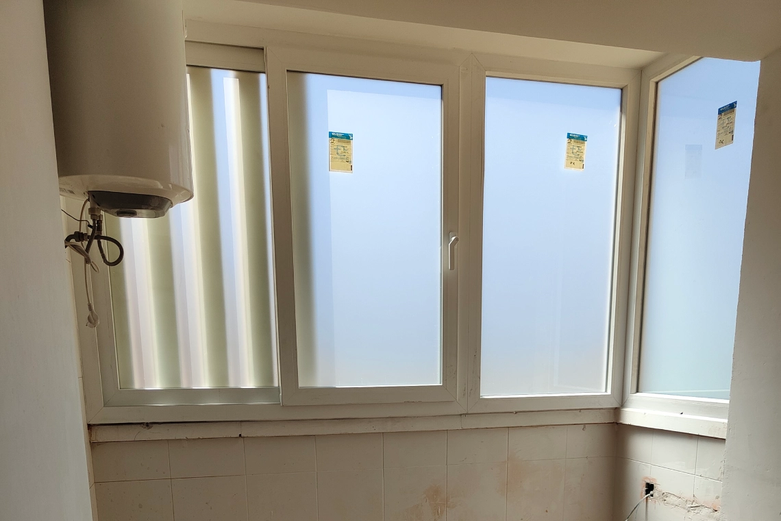 Ventanas de PVC blanco recien colocadas en la galeria de un piso, con las etiquetas de fabrica