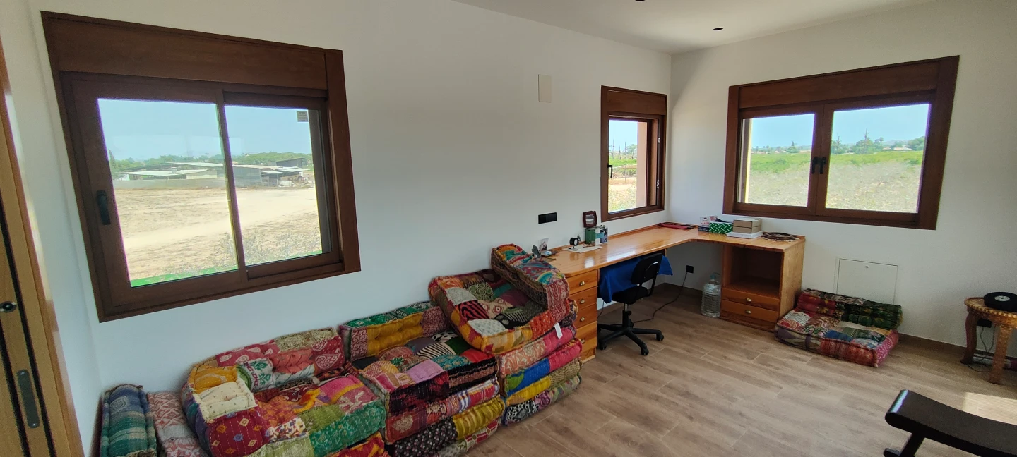 Sala de estar con varias ventanas de aluminio color madera y vistas al campo