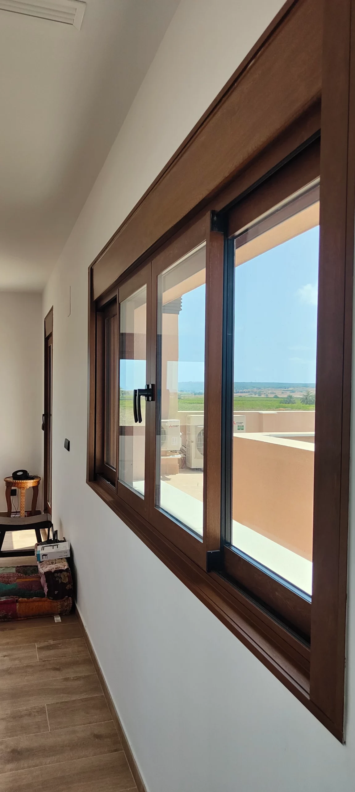 Ventana corredera de aluminio color madera en un pasillo con vistas al mar