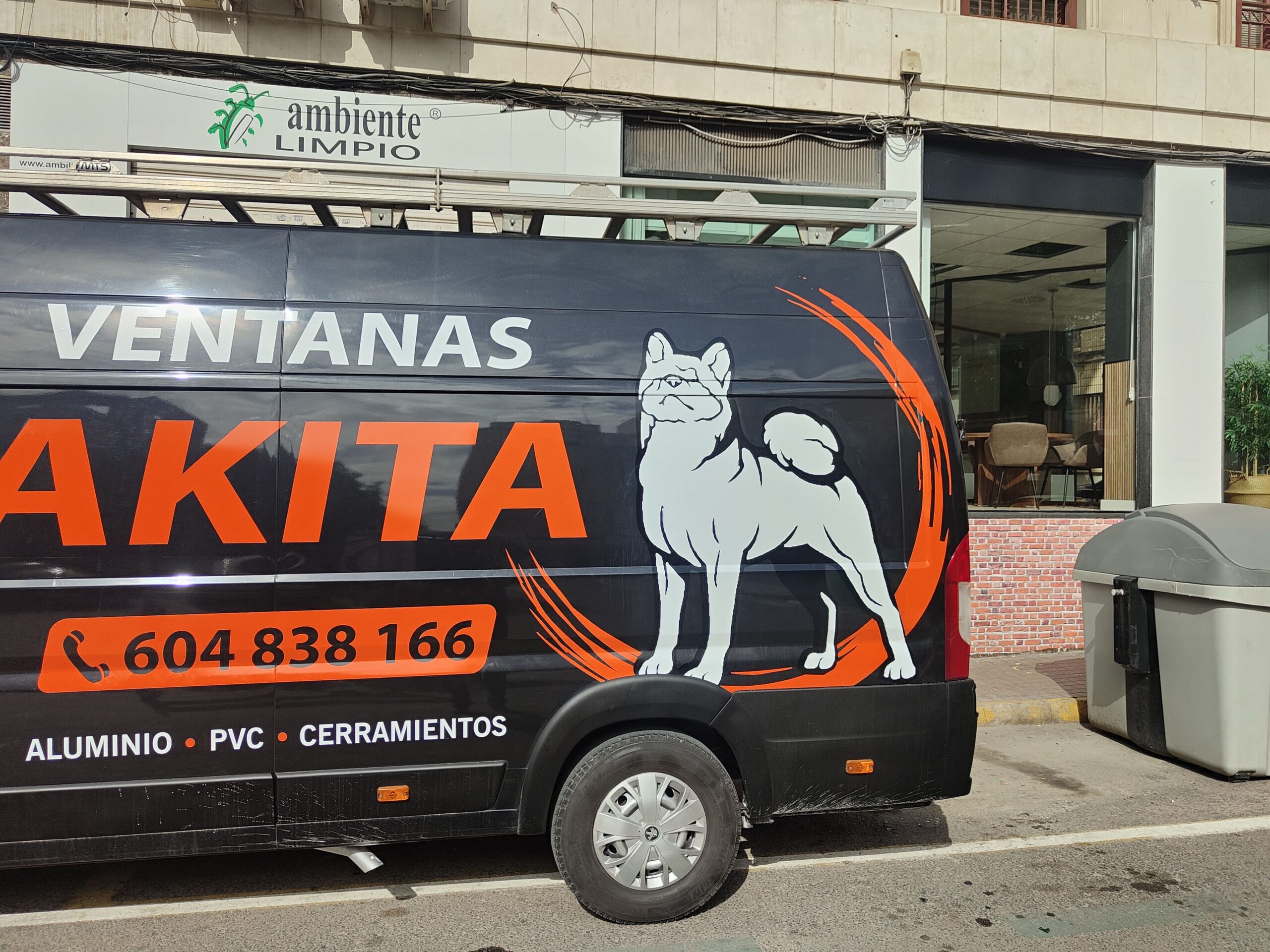 Furgoneta rotulada de Ventanas Akita aparcada en la calle frente a un local
