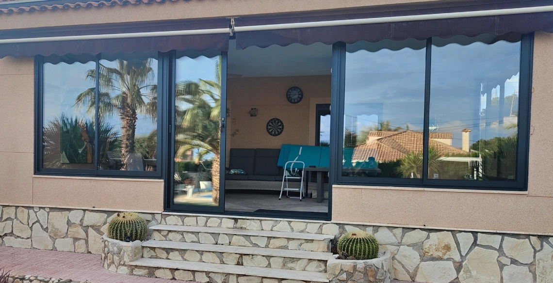 Porche de un chalet cerrado con ventanas de aluminio antracita bajo un toldo
